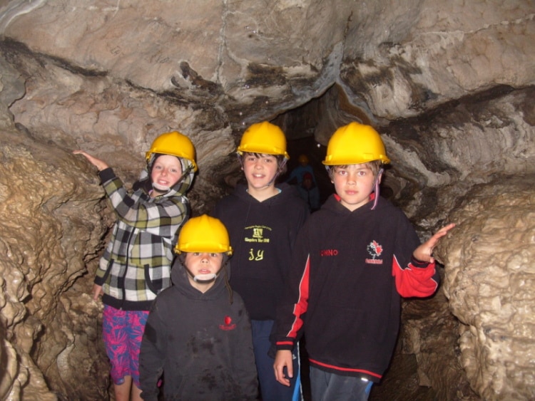 Outdoor Learning Activities For Kids 1 A group of four kids, wearing hard hats, stood smiling in a cave at How Stean Gorge.